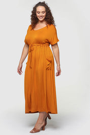 A model wearing the Mila Maxi Dress in colour Tumeric, from the front, showing the whole outfit
