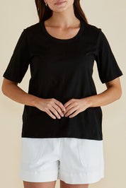 A model wearing the Riley Cotton Tee in colour Black (Black), from the front, cropped image