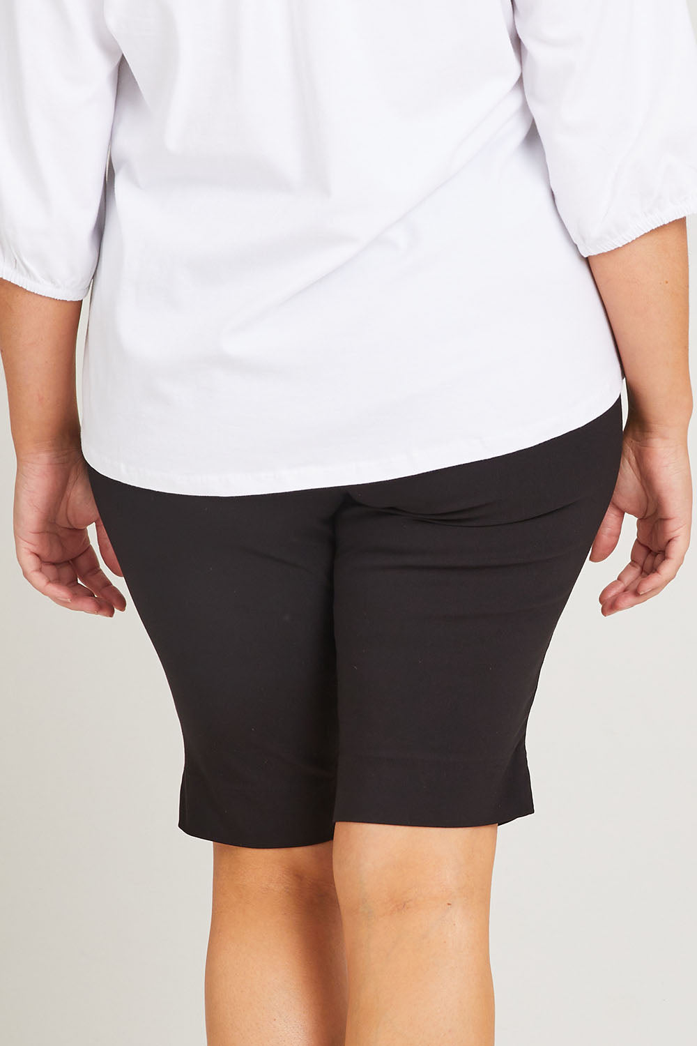 Model Poppy wearing size 16 of the Bermuda Bengaline Short in colour Black (Black), from the back