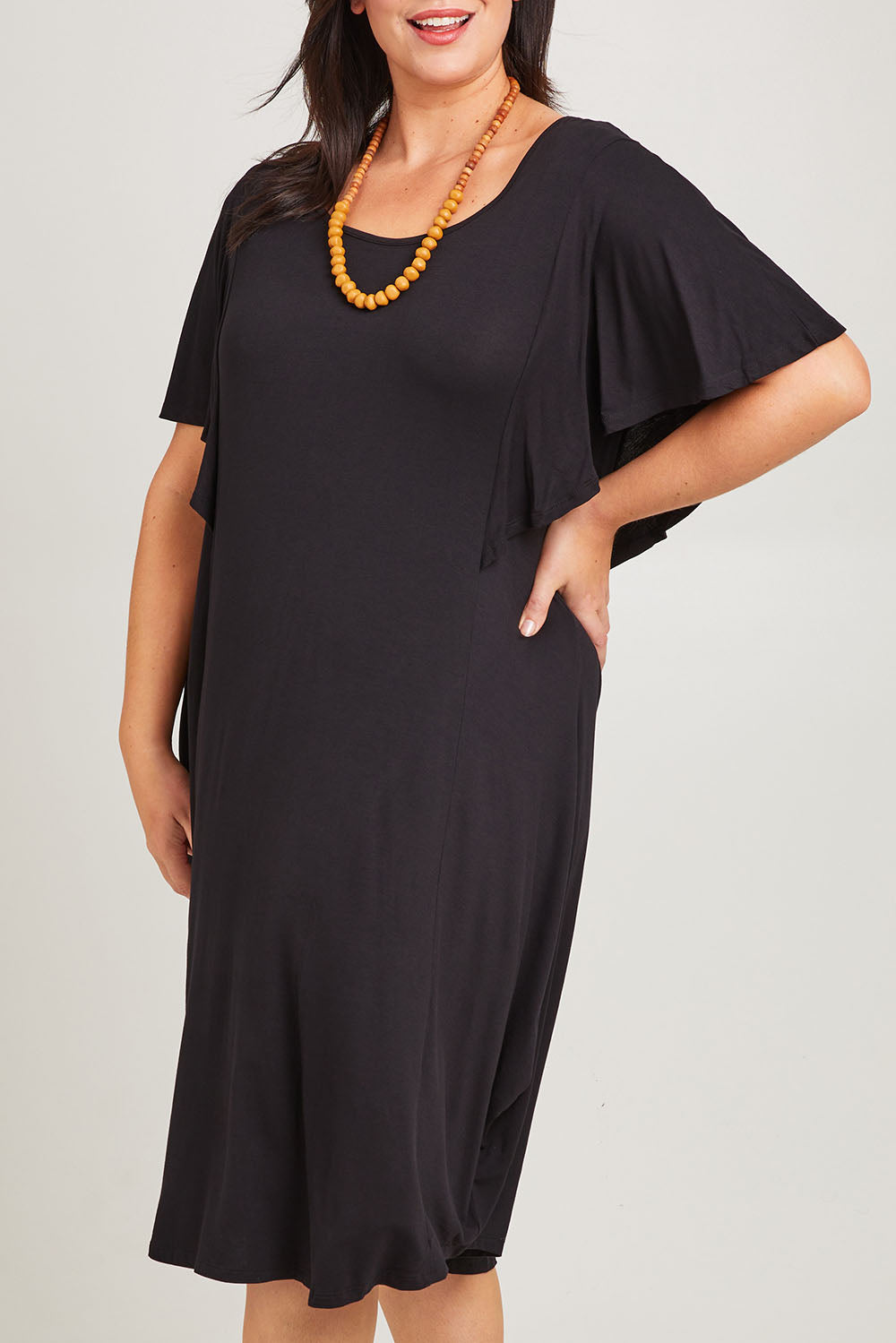 Model Poppy wearing size 16 of the Tahiti Frill Dress in colour Black (Black), from the front, cropped image