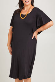 Model Poppy wearing size 16 of the Tahiti Frill Dress in colour Black (Black), from the front, cropped image