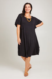 Model Poppy wearing size 16 of the Tahiti Frill Dress in colour Black (Black), from the front, showing the whole outfit