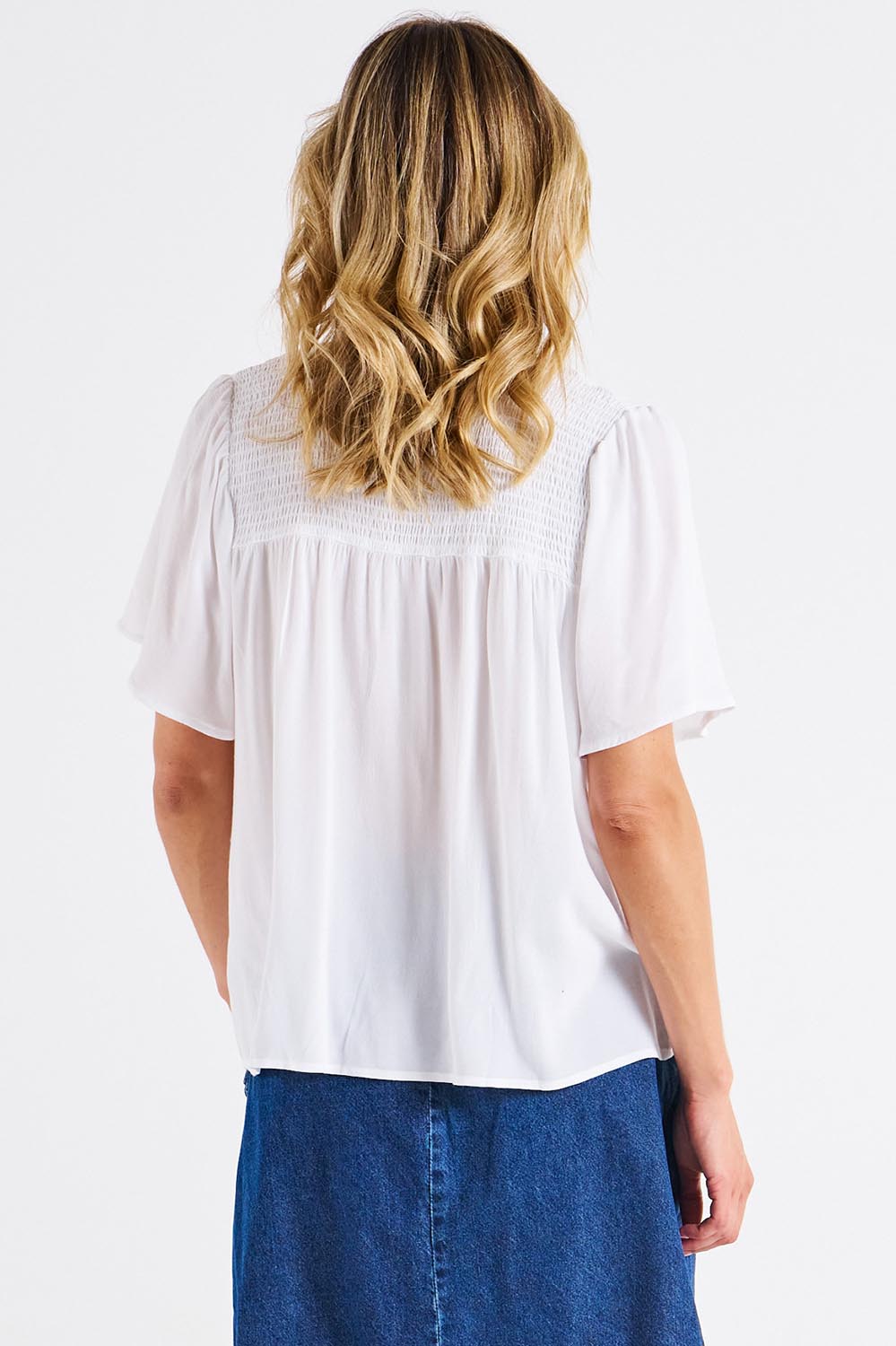 A model wearing the Sandy Shirred Blouse in colour White (White), from the back