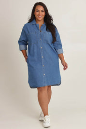 Model Ashleigh wearing size 16 of The Denim Shacket Dress With Pockets in colour Denimblue (Blue), from the front, showing the whole outfit