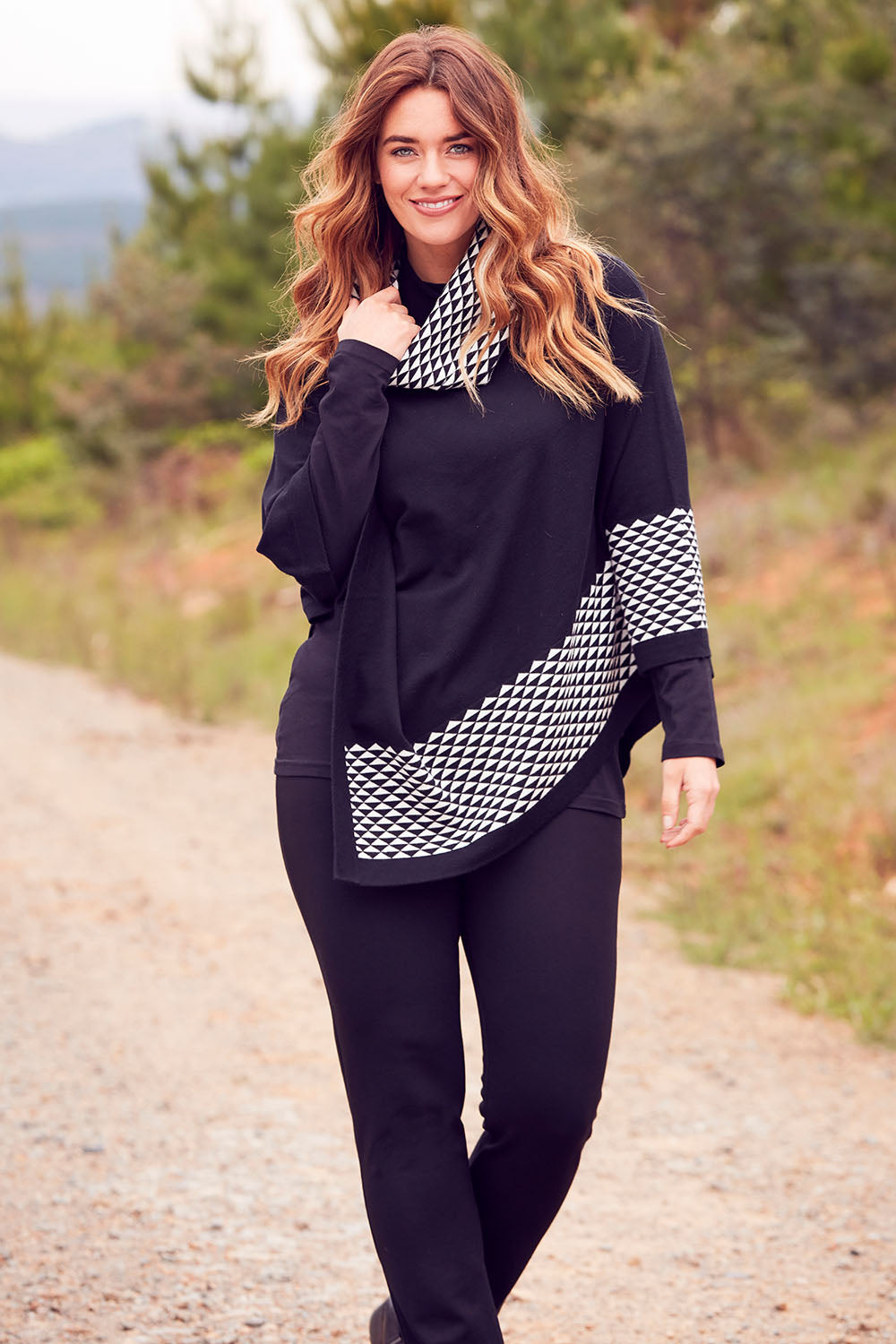 Model Laura wearing size M-L of The Patterned Removable Roll Neck Poncho in colour Blackprint (Black), from the front, showing the whole outfit