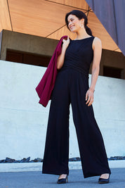 Model Miranda wearing size 10 of The Cross Waist Jumpsuit in colour Black (Black), from the front, showing the whole outfit