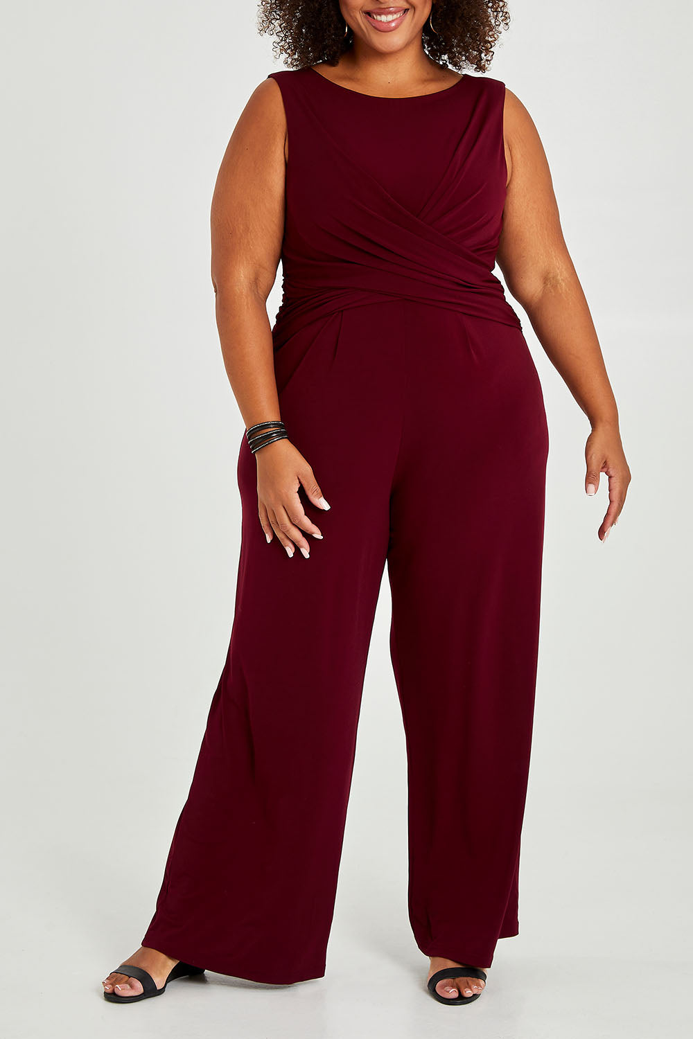 Model Alexis wearing size 18 of The Cross Waist Jumpsuit in colour Port (Purple), from the front, cropped image