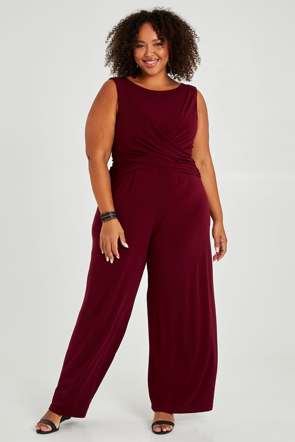 Model Alexis wearing size 18 of The Cross Waist Jumpsuit in colour Port (Purple), from the front, showing the whole outfit