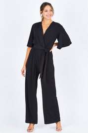 Model Madeline wearing size 10 of The Bell Sleeve Jumpsuit in colour Black (Black), from the front, showing the whole outfit