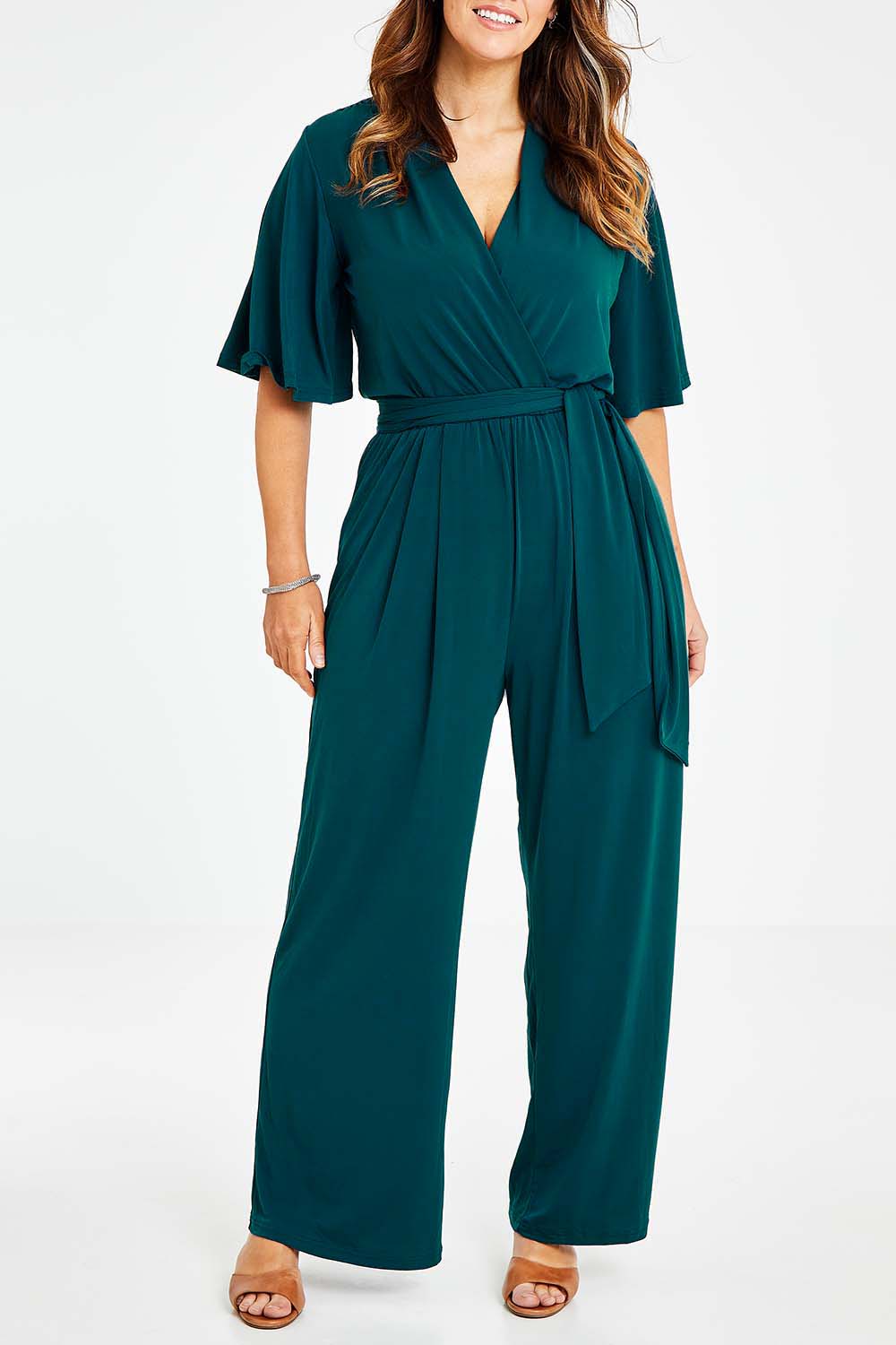 Model Laura wearing size 14 of The Bell Sleeve Jumpsuit in colour Darkteal (Green), from the front, cropped image