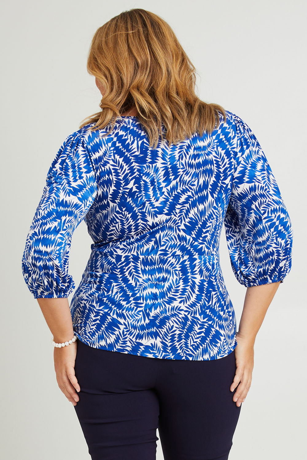 Model Fiona wearing size 18 of The Printed Knot Waist Detail Blouse in colour Fern (Blue), from the back