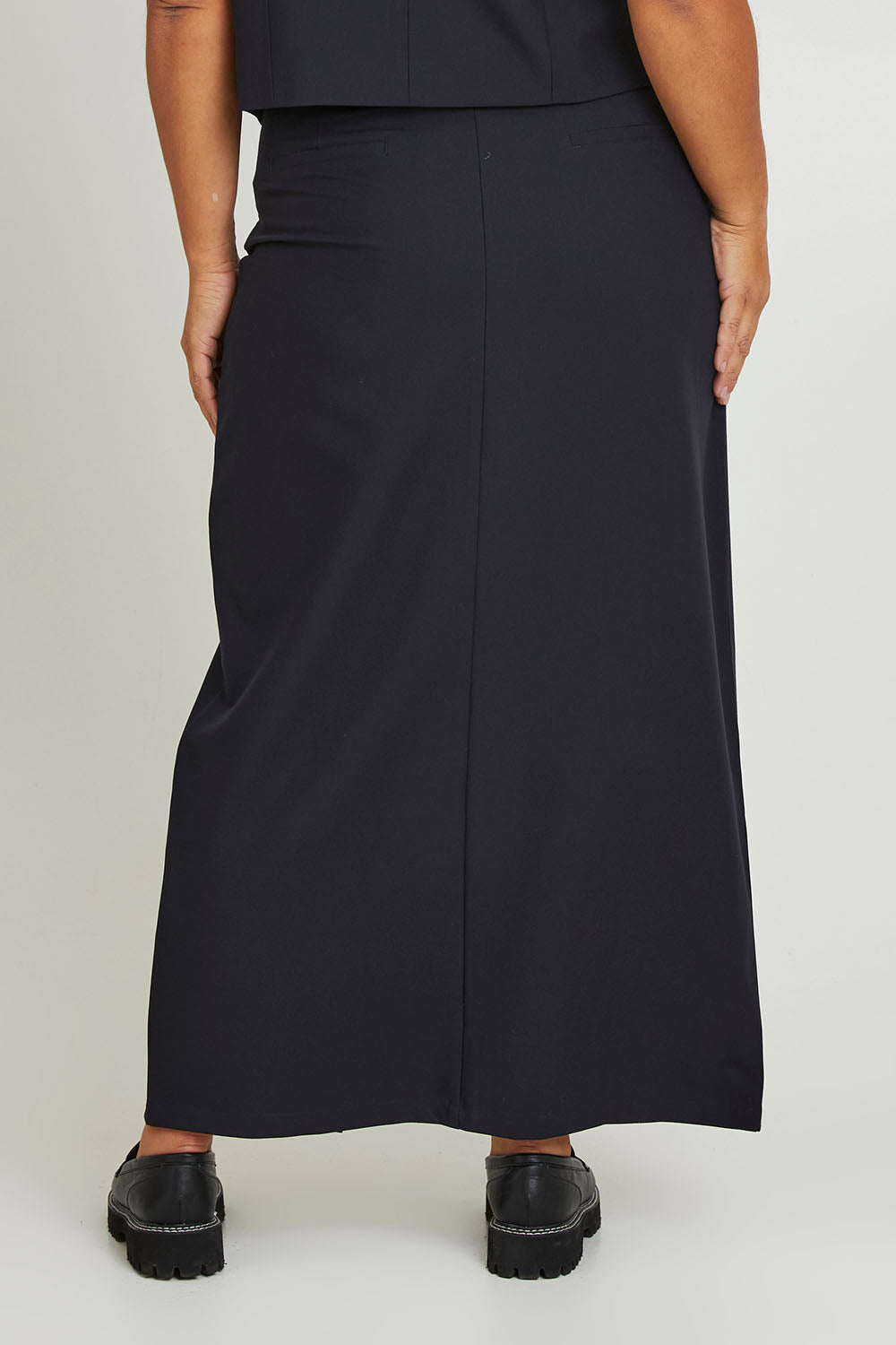 Model Ashleigh wearing size 16 of The Tailored Maxi Skirt in colour Ink (Blue), from the back