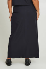 Model Ashleigh wearing size 16 of The Tailored Maxi Skirt in colour Ink (Blue), from the back