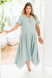 Model Palatina wearing size 16 of the Belle Angled Hem Dress in colour Sage (Green), from the front, showing the whole outfit