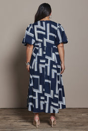 Model Ashleigh wearing size 16 of the Belle Printed Twist Knot Detail Cotton Dress in colour Bluegeo (Blue), from the back