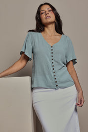 Model Tahnee wearing size 10 of the Cute As A Button Blouse in colour Sage (Green), from the front, cropped image