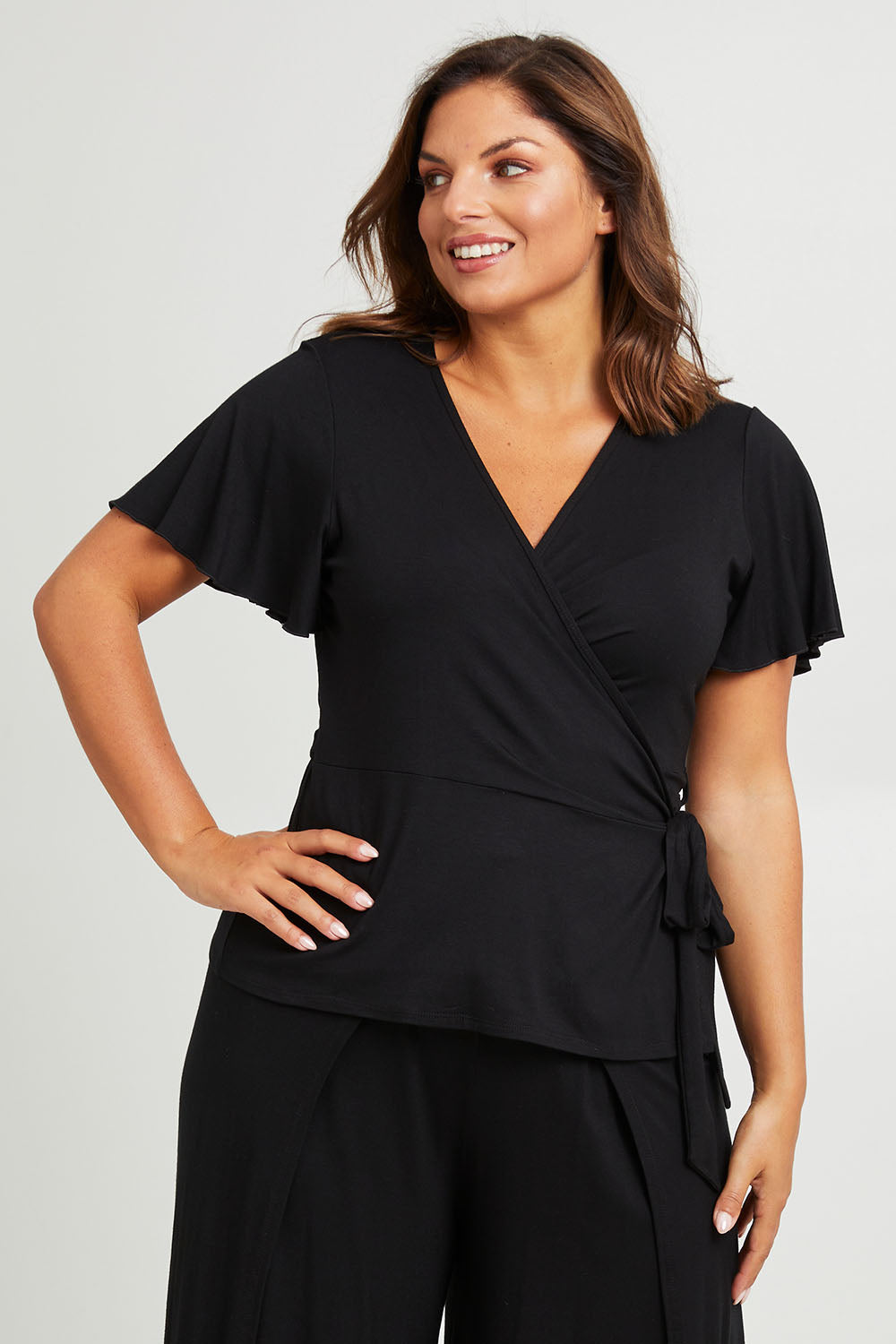 Model Monique wearing size 14 of the All For You Wrap Top in colour Black (Black), from the front, cropped image