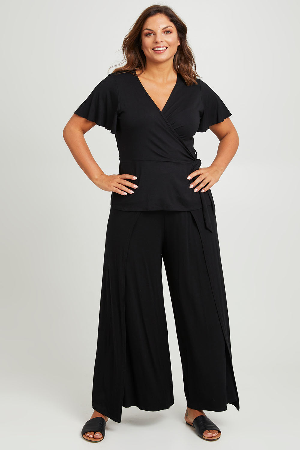 Model Monique wearing size 14 of the All For You Wrap Top in colour Black (Black), from the front, showing the whole outfit