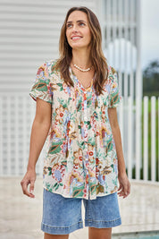 Model Tegand wearing size 10 of the Sunny Day Pleated Short Sleeve Blouse – Fleur in colour Fleur, from an angle