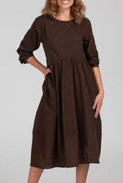A model wearing the Guru Cotton Dress in colour Coffee, from the front, cropped image