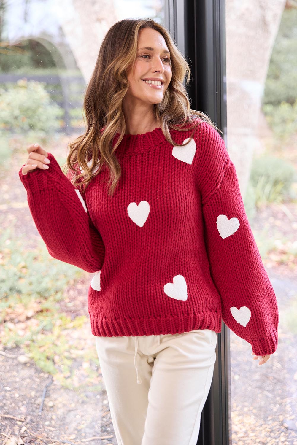 A model wearing the Heart On My Sleeve Knit in colour Cherrywhit (Red), from the front, showing the whole outfit