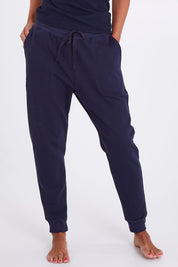 Model Alex wearing the Nova Pant in colour Navy (Blue), from the front, cropped image