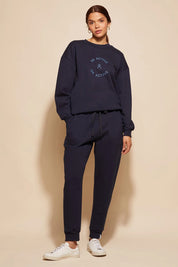 A model wearing the Nova Pant in colour Navy (Blue), from the front, showing the whole outfit