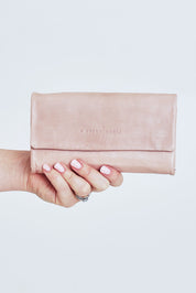 Model Steph wearing size OneSize of the Rose Leather Purse in colour Duskypink (Pink), from the front, cropped image