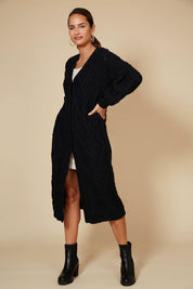 A model wearing the Howie Cable Cardigan in colour Ebony (Black), from the front, showing the whole outfit