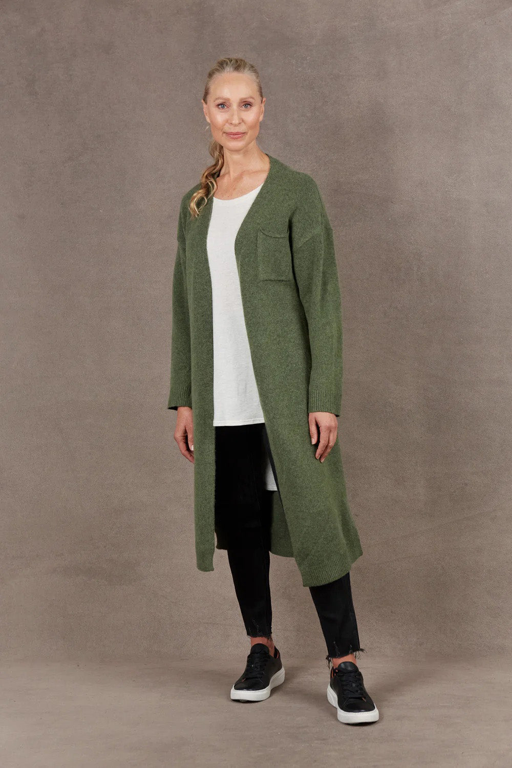 A model wearing the Paarl Longline Cardigan in colour Moss (Green), from the front, showing the whole outfit