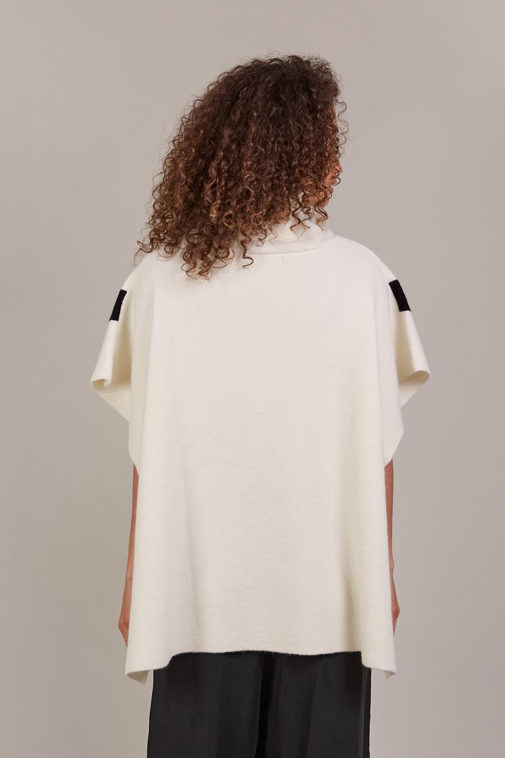 A model wearing the Avino Poncho in colour Ecru, from the back