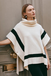 A model wearing the Avino Poncho in colour Ecru, from the front, showing the whole outfit
