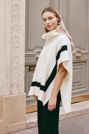 A model wearing the Avino Poncho in colour Ecru, from the front, showing the whole outfit