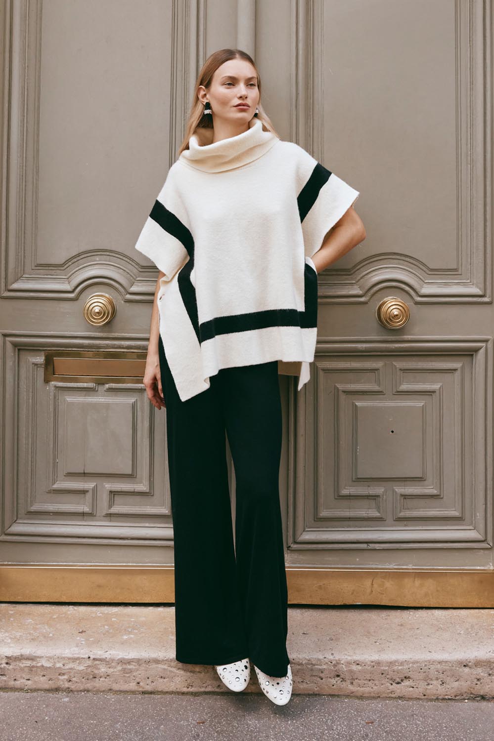 A model wearing the Avino Poncho in colour Ecru, from the front, showing the whole outfit