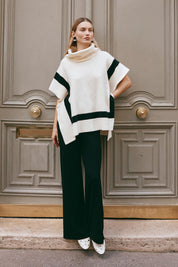 A model wearing the Avino Poncho in colour Ecru, from the front, showing the whole outfit