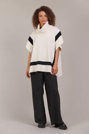 A model wearing the Avino Poncho in colour Ecru, from the front, showing the whole outfit