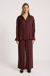 A model wearing the Calista Shirt in colour Mahogany (Red), from the front, showing the whole outfit