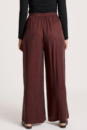 A model wearing the Calista Pant in colour Mahogany (Red), from the back