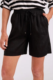 Model Genericm wearing size sample of the Studio Linen Bermuda Short – Black in colour Black, from an angle