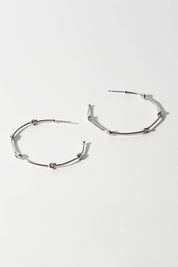 A model wearing size OneSize of the Knots Of Freedom Hoop Earrings in colour Steel (Metallics), from the front, showing the whole outfit