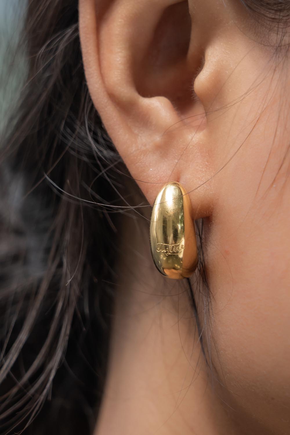 A model wearing the Love & Justice Half Hoop Earrings in colour Gold (Metallics), from the front, cropped image