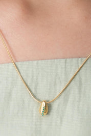 A model wearing the Radicle Drop Necklace in colour Gold (Metallics), from the front, cropped image