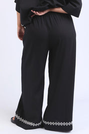 A model wearing the Nina Embroidered Pant in colour Black (Black), from the back