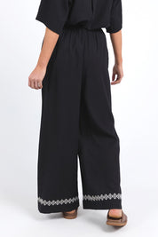 A model wearing the Nina Embroidered Pant in colour Black (Black), from the back