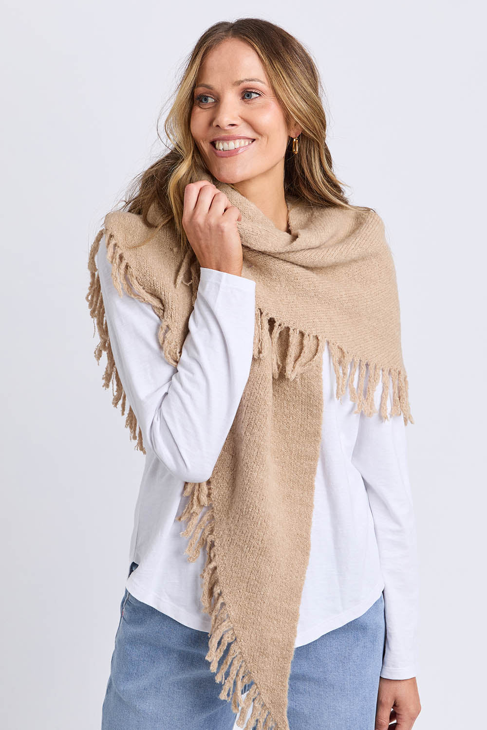 A model wearing the Fringed Triangle Scarf in colour Oatmeal, from the front, cropped image
