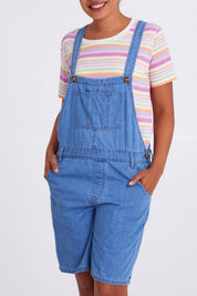 Model Olivia wearing size 10 of the Maltilda Short Denim Overalls in colour Midblue (Blue), from the front, cropped image