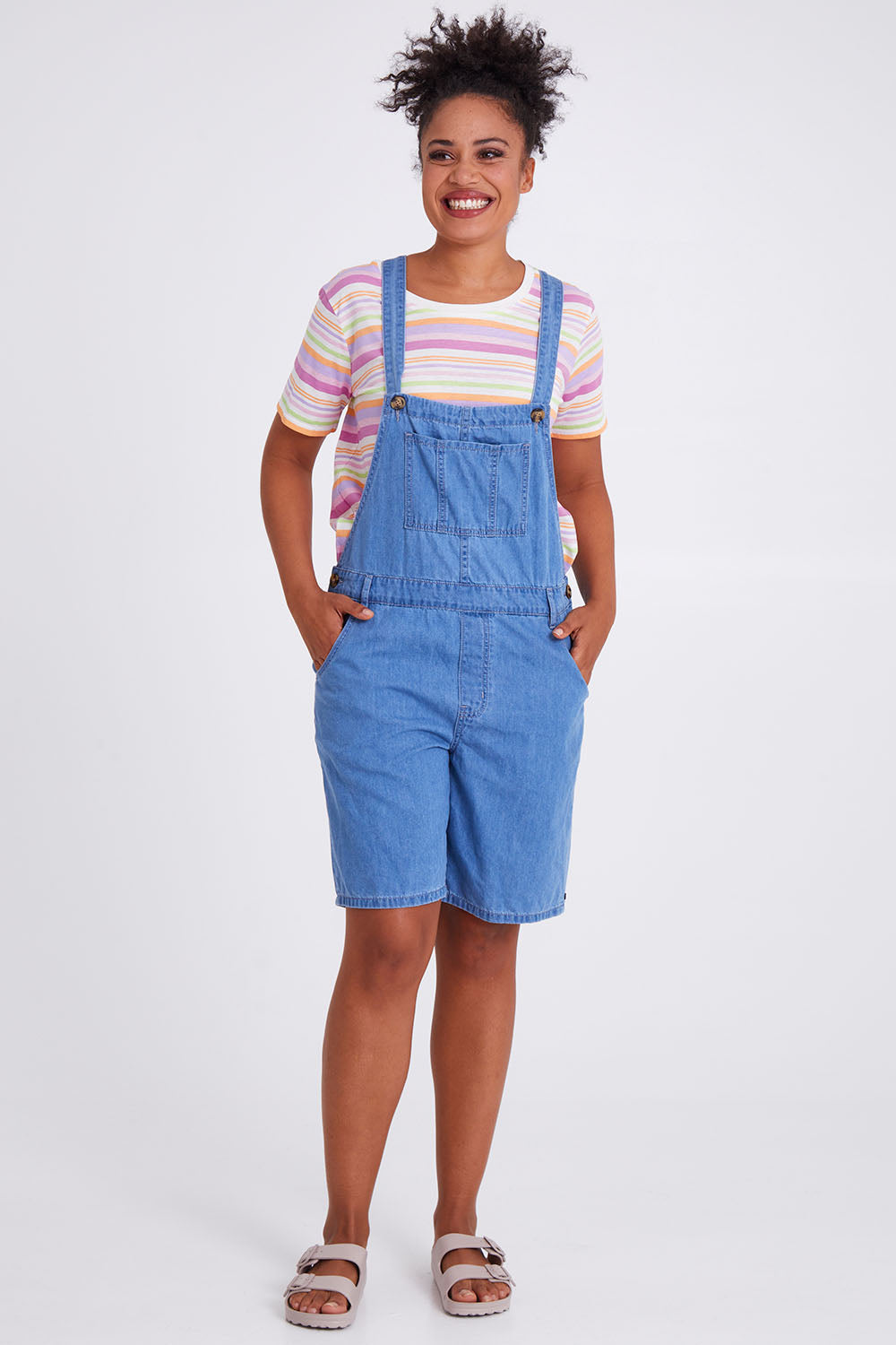 Model Olivia wearing size 10 of the Maltilda Short Denim Overalls in colour Midblue (Blue), from the front, showing the whole outfit