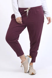 A model wearing the Fundamental Brunch Cotton Pant in colour Merlot (Red), from the front, cropped image