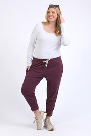 A model wearing the Fundamental Brunch Cotton Pant in colour Merlot (Red), from the front, showing the whole outfit