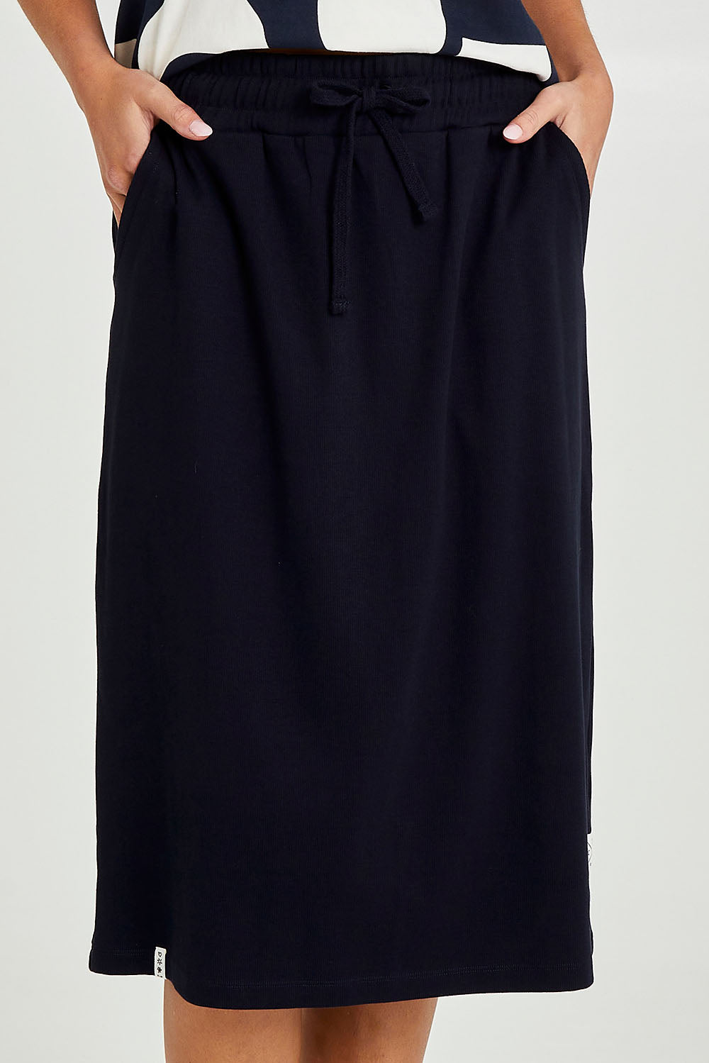 Model Madeline wearing size 10 of the Fundamental Rib Midi Skirt in colour Navy (Blue), from the front, cropped image